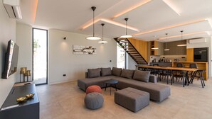 Uma sala de estar moderna com sofá seccional, pufes, área de jantar e cozinha, com uma escada.