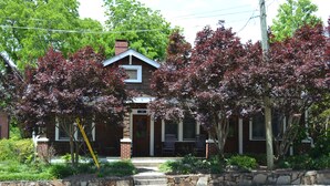 A two-story house with a stone foundation, a front porch with chairs, and a chimney.