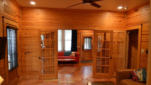 A log cabin interior with a red couch, wooden walls, and a tiled floor.