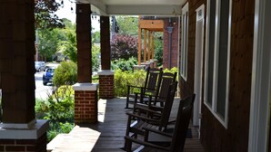 A wooden porch with brick pillars, wooden chairs, and a view of a street with cars and greenery.
