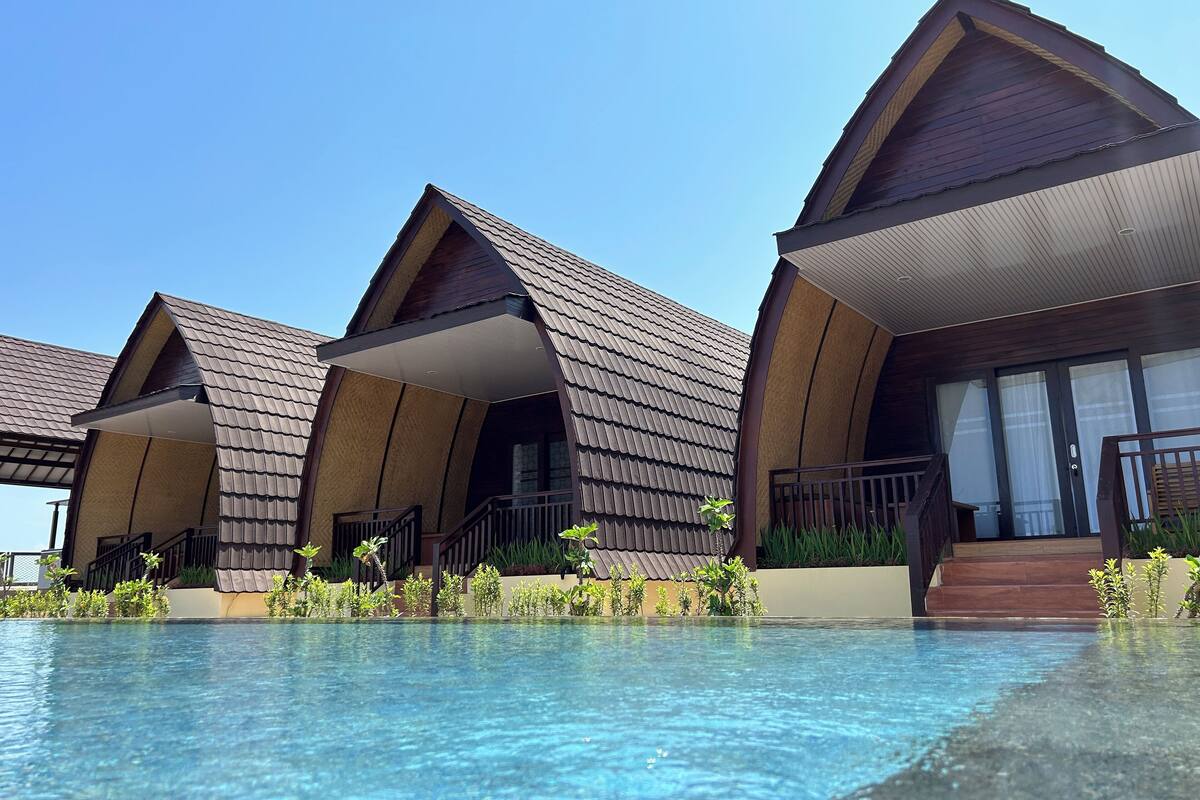 A resort with multiple bungalow-style rooms, a swimming pool, and a clear blue sky.
