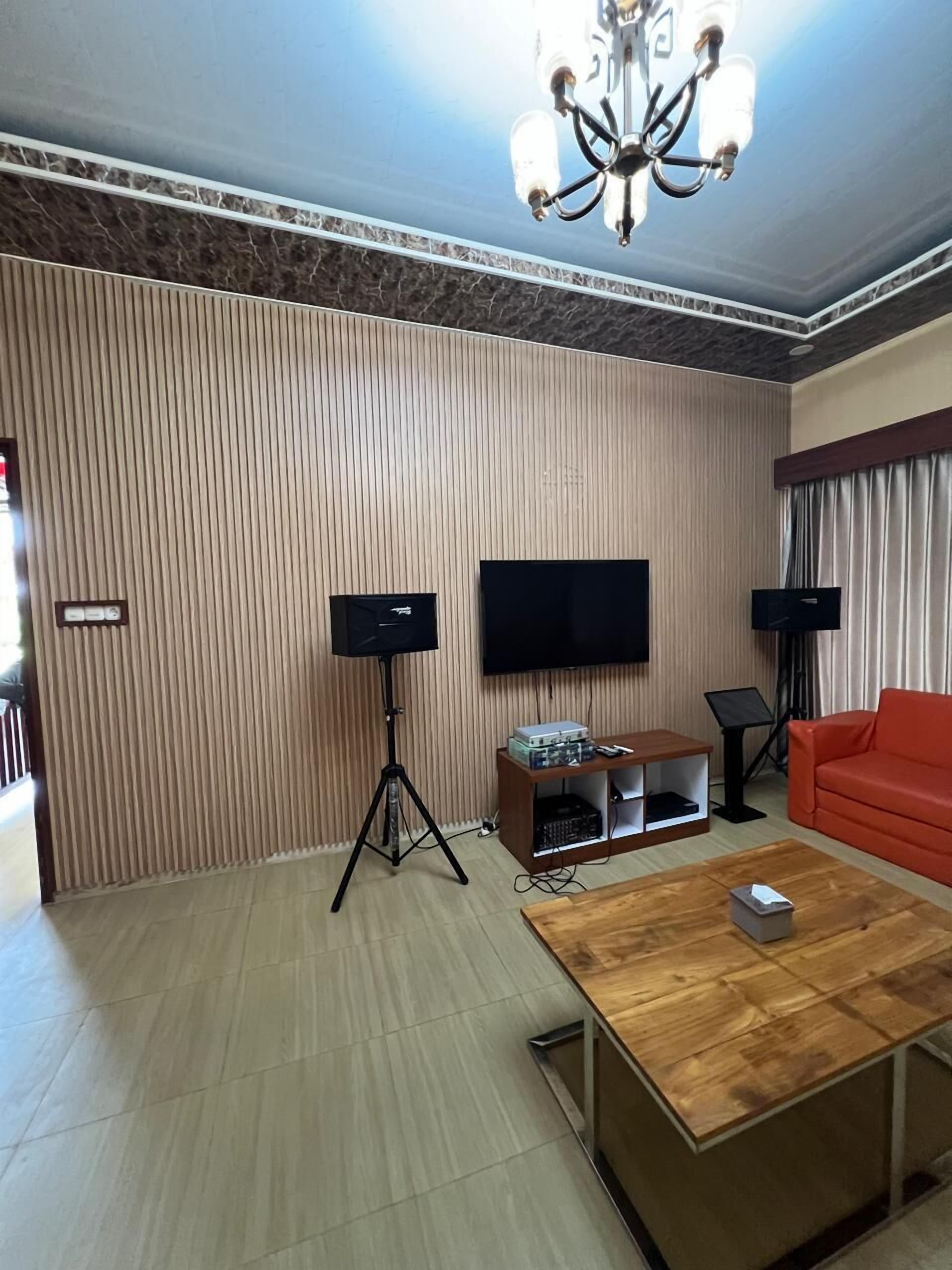 Een woonkamer met een flatscreen televisie, twee staande speakers, een houten salontafel en een rode bank.