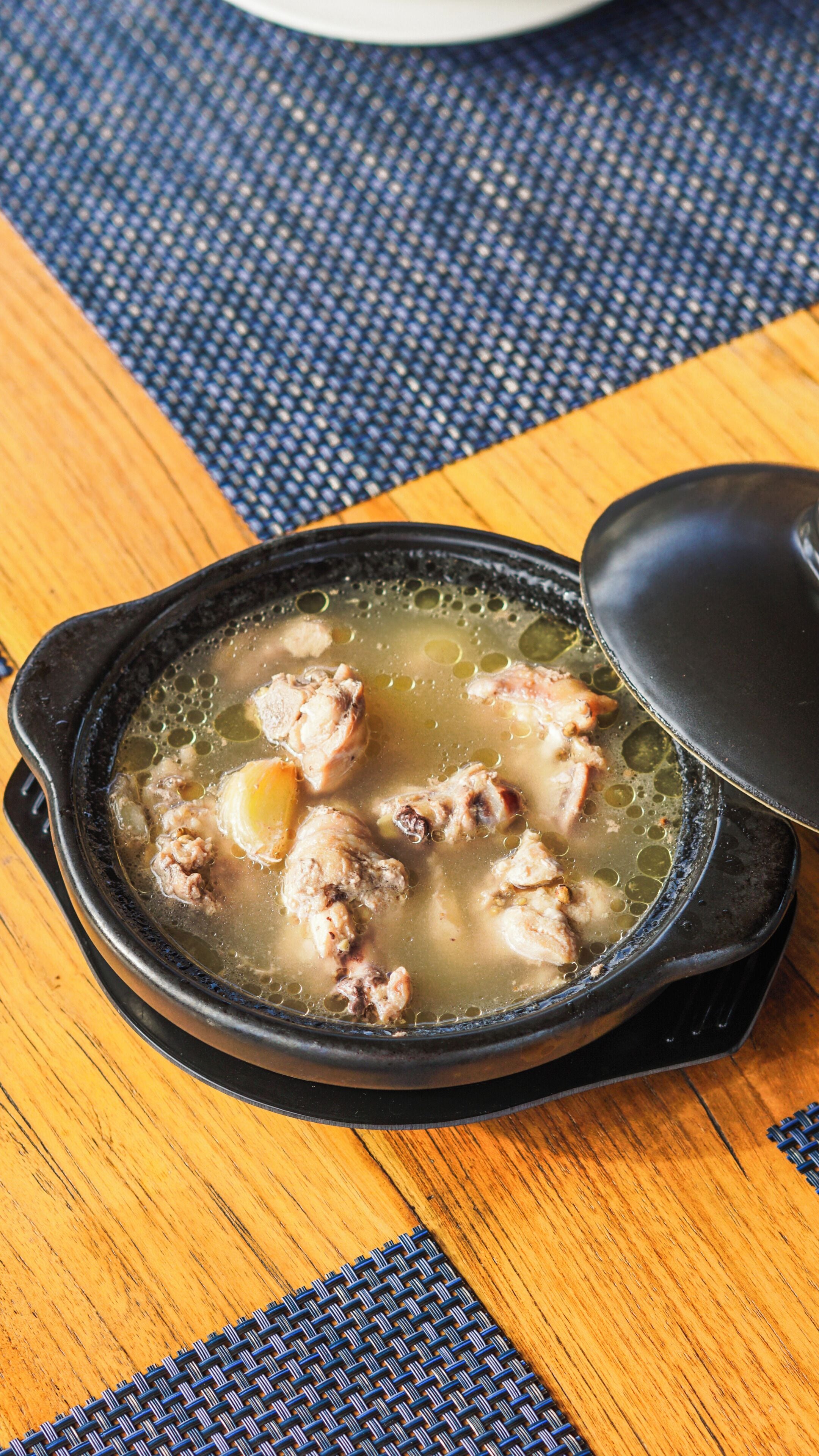 A cast iron pot with a lid, containing a broth with meat and vegetables, on a wooden table.