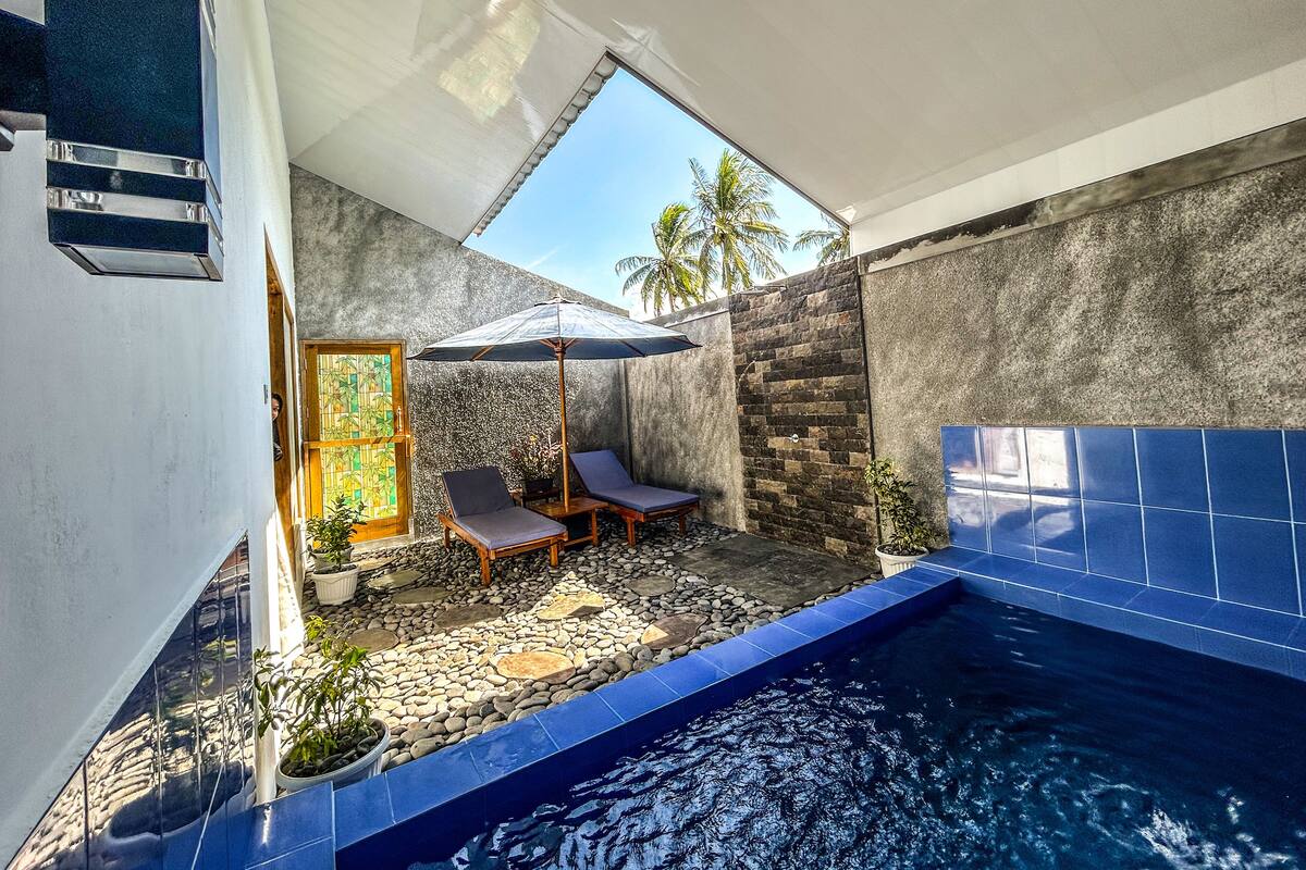 A swimming pool with a stone and blue tiled edge, surrounded by lounge chairs and a potted plant.