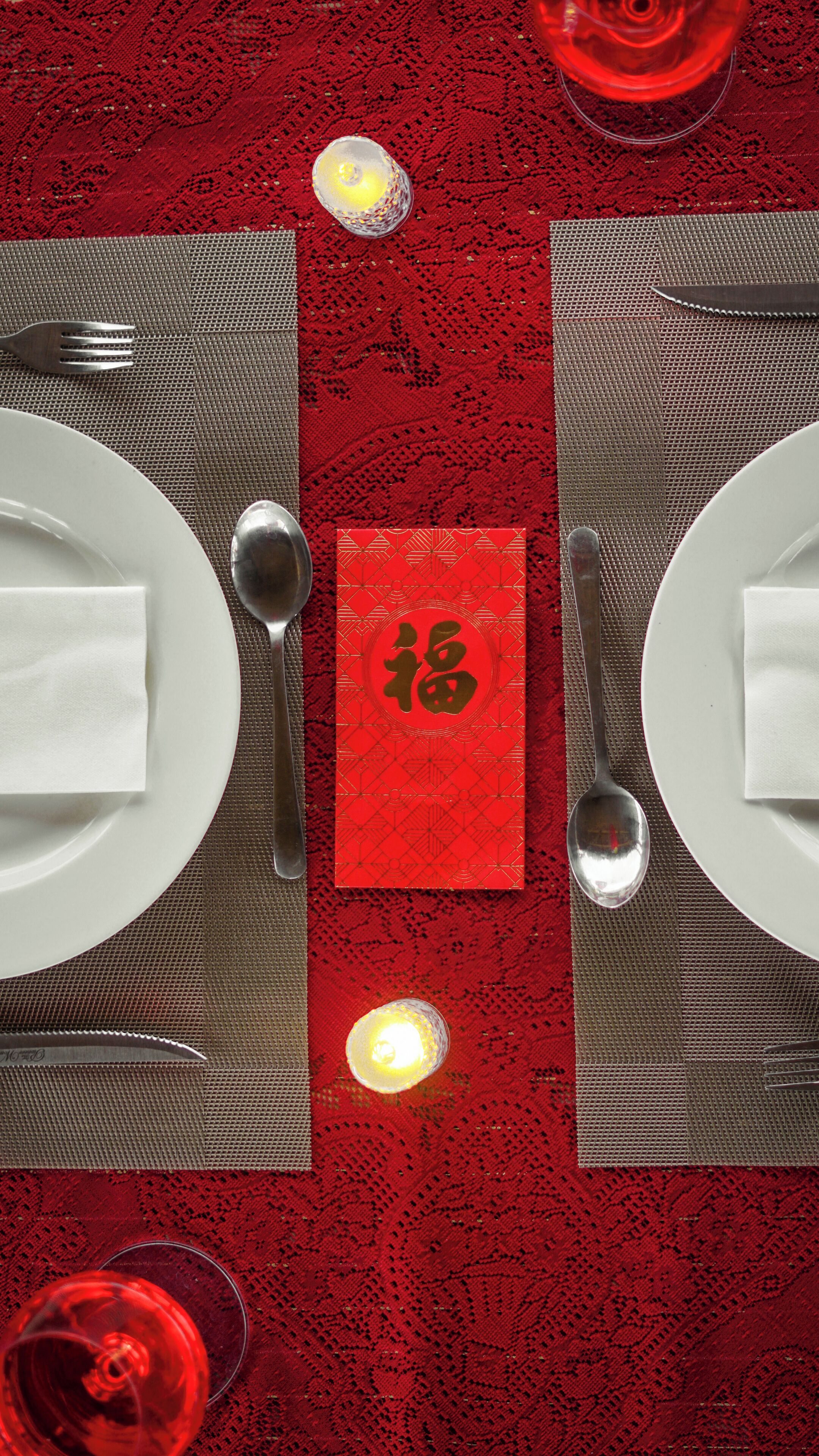 Una mesa para dos con mantel individual rojo, platos blancos, cubiertos y una tarjeta roja con caracteres chinos.