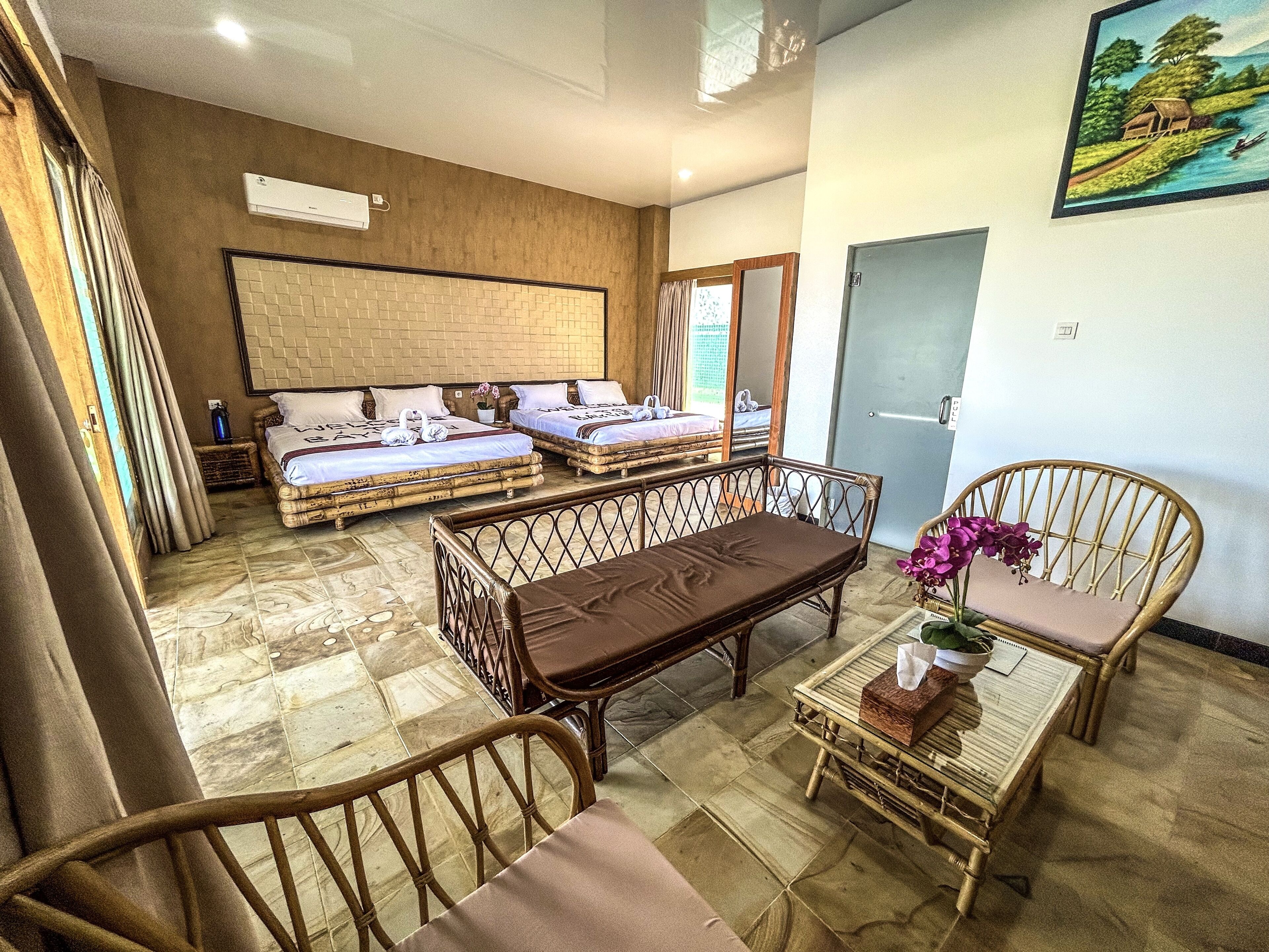 Habitación de hotel con dos camas, una mesa de comedor, sillas, una mesita con un florero y un cuadro en la pared.