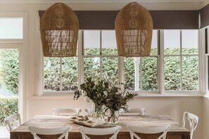 Un comedor con mesa de madera, sillas blancas y un florero con flores.