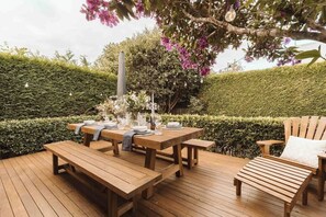 Una terraza de madera al aire libre con una mesa lista para comer, rodeada de bancos y sillas.