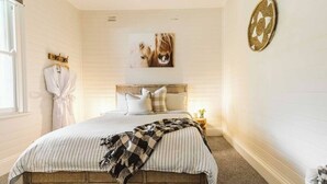 A bedroom with a wooden bed frame, striped bedding, a headboard with pillows, a wall-mounted artwork of a lion, and a small bedside table with a lamp. - 'Blooms At Berry' - Luxury in the Heart of Berry (Berry)
