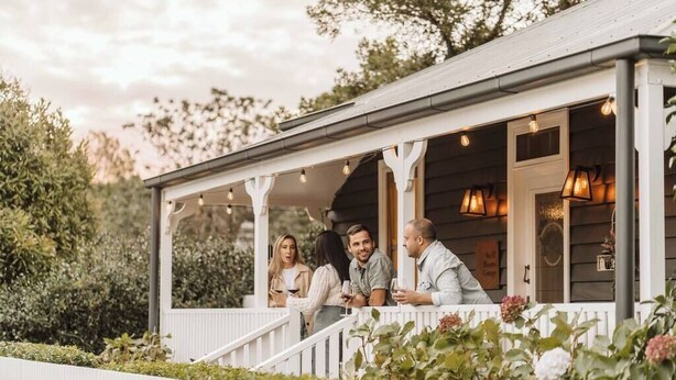 A covered porch with people standing and conversing, surrounded by greenery and a white fence. - 'Blooms At Berry' - Luxury in the Heart of Berry (Berry)