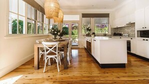 A modern kitchen with a large island, white cabinetry, and a dining area with a wooden table and chairs. - 'Blooms At Berry' - Luxury in the Heart of Berry (Berry)
