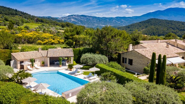 Eine Villa mit Swimmingpool, umgeben von üppigem Grün und Bergen im Hintergrund.
