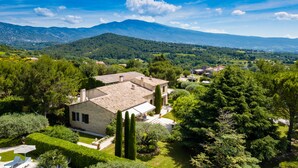 Eine Villa mit Steinziegeldach, umgeben von üppiger Vegetation und einer Berglandschaft im Hintergrund.