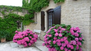 Ein Steinhaus mit zwei großen Kübeln voller rosa Blüten.