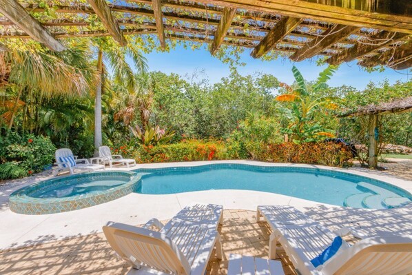 A swimming pool with a tiled edge, surrounded by lounge chairs and a pergola.