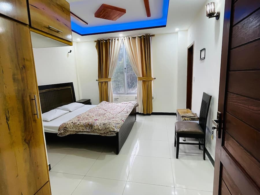 A bedroom with a bed, a chair, a wardrobe, and a window with curtains.