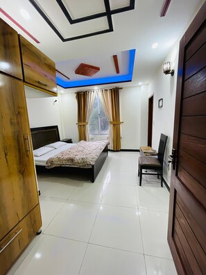 A bedroom with a bed, a chair, a wardrobe, and a window with curtains. - Paradise View Hotel And Restaurant (Khaira Gali)