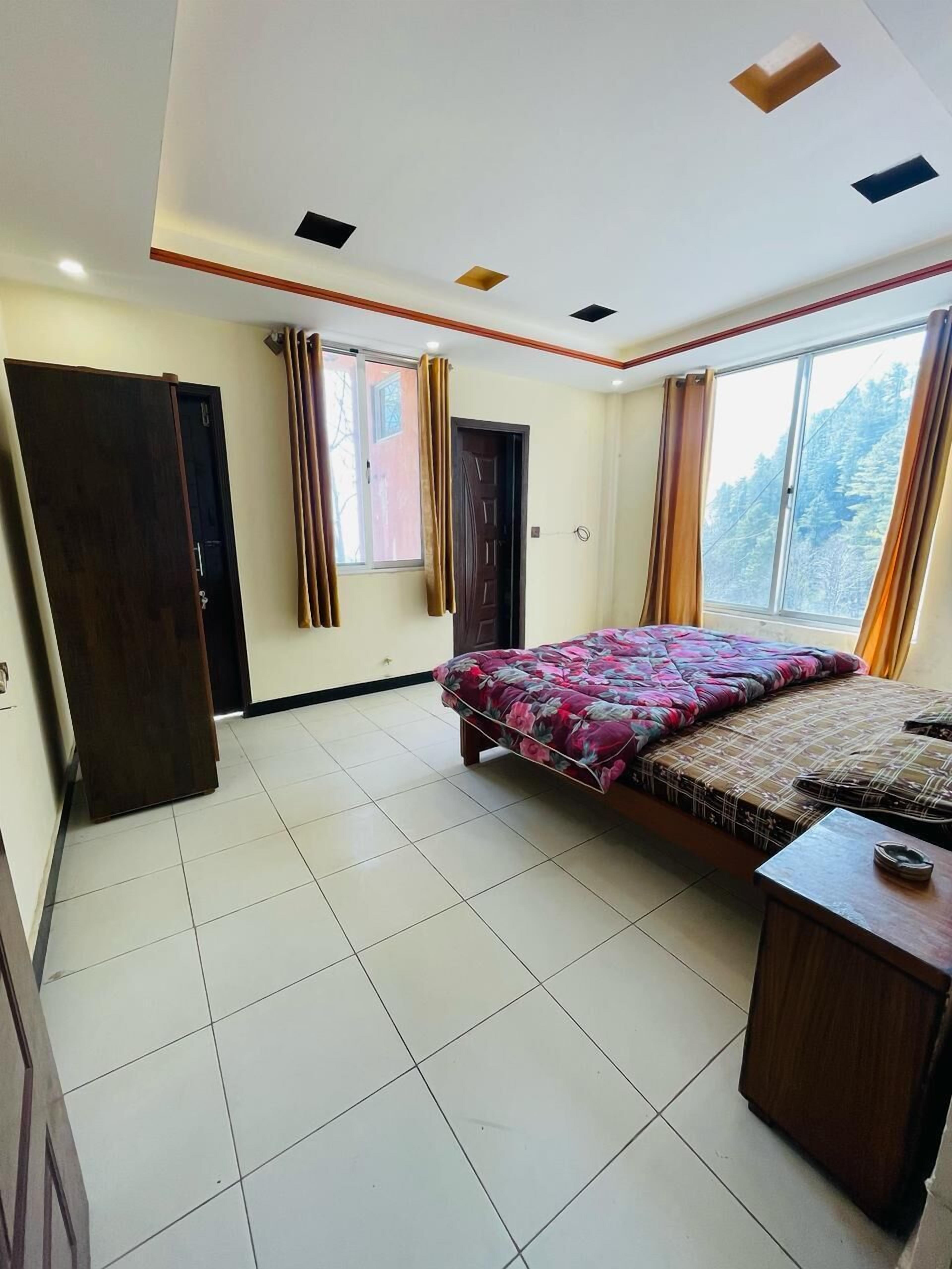Quarto com uma cama, mesa de cabeceira de madeira, janela com cortinas e porta.