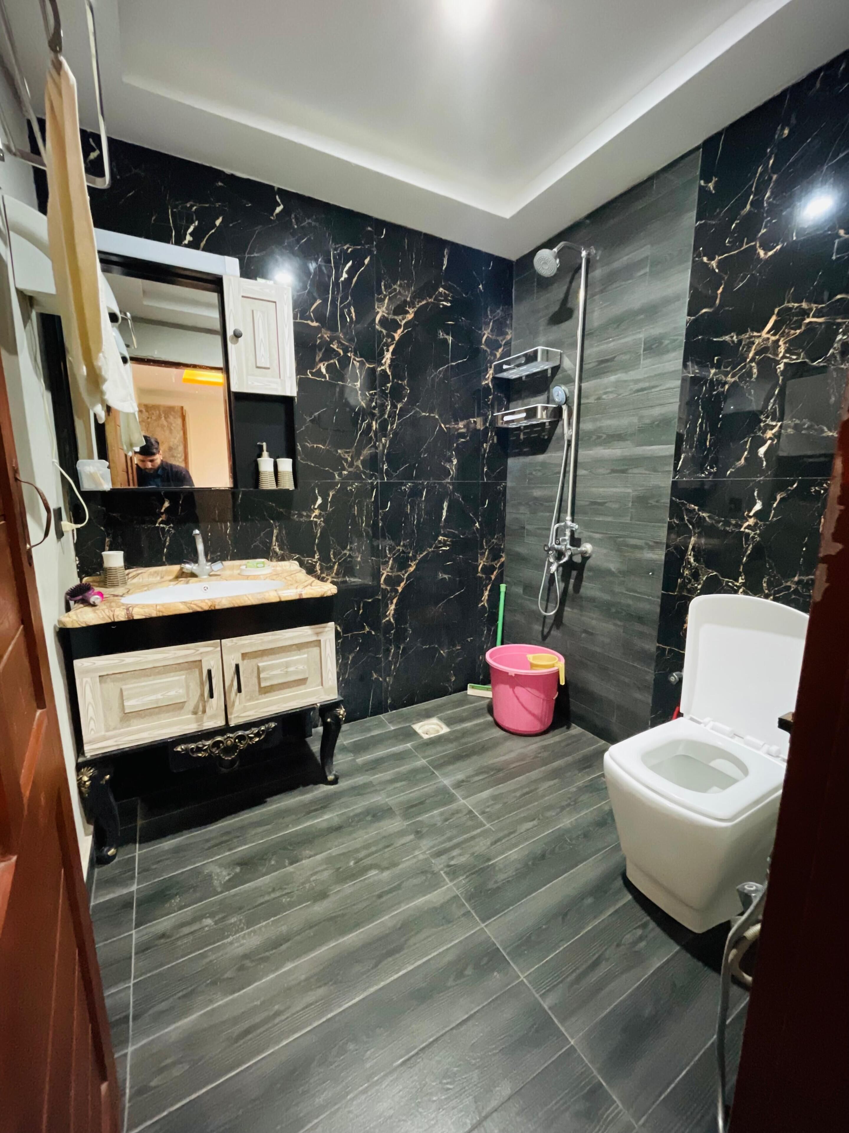 Een moderne badkamer met een wand van zwart marmer, een wit toilet, een wastafel met spiegel en een douche.