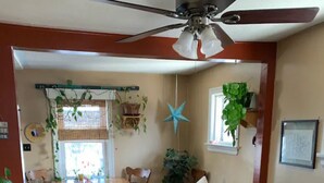 A cozy living room with a wooden floor, a black sofa, a ceiling fan, and a dining area with wooden chairs and a table. - Vacation home you’ll enjoy (Lower Sackville)