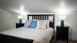 A bedroom with a bed, two bedside tables, and a nightstand. - Vacation home you’ll enjoy (Lower Sackville)