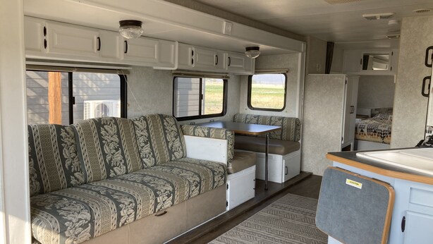 A compact RV interior with a sofa, kitchenette, and a small dining area. - Camper/RV @ The Rendezvous - Wi-Fi, fire pit, A/C (Cody)