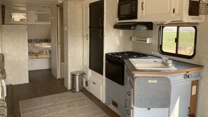 A compact RV kitchen with a stove, microwave, sink, and a window offering a view of the outdoors. - Camper/RV @ The Rendezvous - Wi-Fi, fire pit, A/C (Cody)