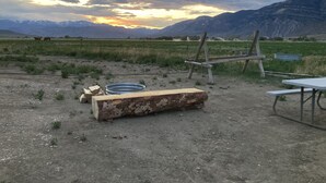 A rustic outdoor setting with a wooden bench, a metal basin, and a table, set against a backdrop of mountains and a cloudy sky. - Camper/RV @ The Rendezvous - Wi-Fi, fire pit, A/C (Cody)