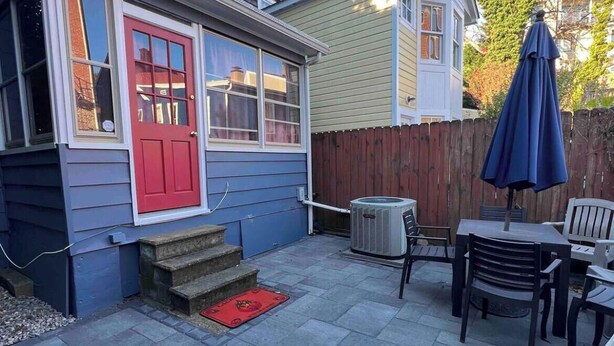 Un cortile residenziale con una porta rossa, un patio con piastrelle in pietra, una recinzione in legno e un ombrellone blu.
