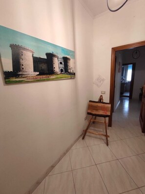 A hallway with a large painting of a castle, a wooden easel with a canvas, and a tiled floor. - Vanna House (Torre del Greco)