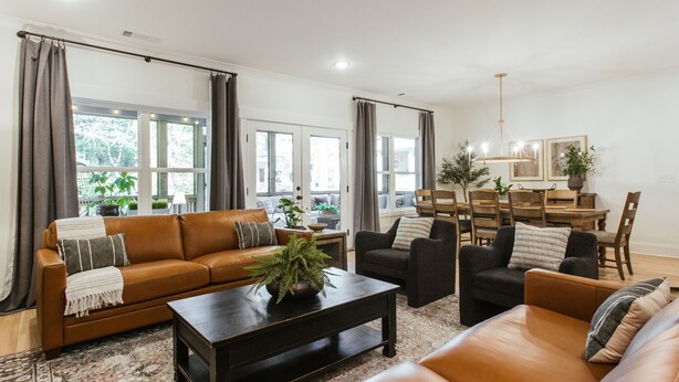 A modern living room with a brown leather sofa, a black coffee table, and a dining area with a wooden table and chairs.