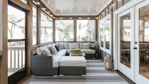 Ein überdachter Balkon mit einer Eckcouch, einem Deckenventilator und großen Fenstern.