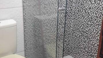 Ein Badezimmer mit Toilette, einer Duschkabine aus Glas und gefliesten Wänden.
