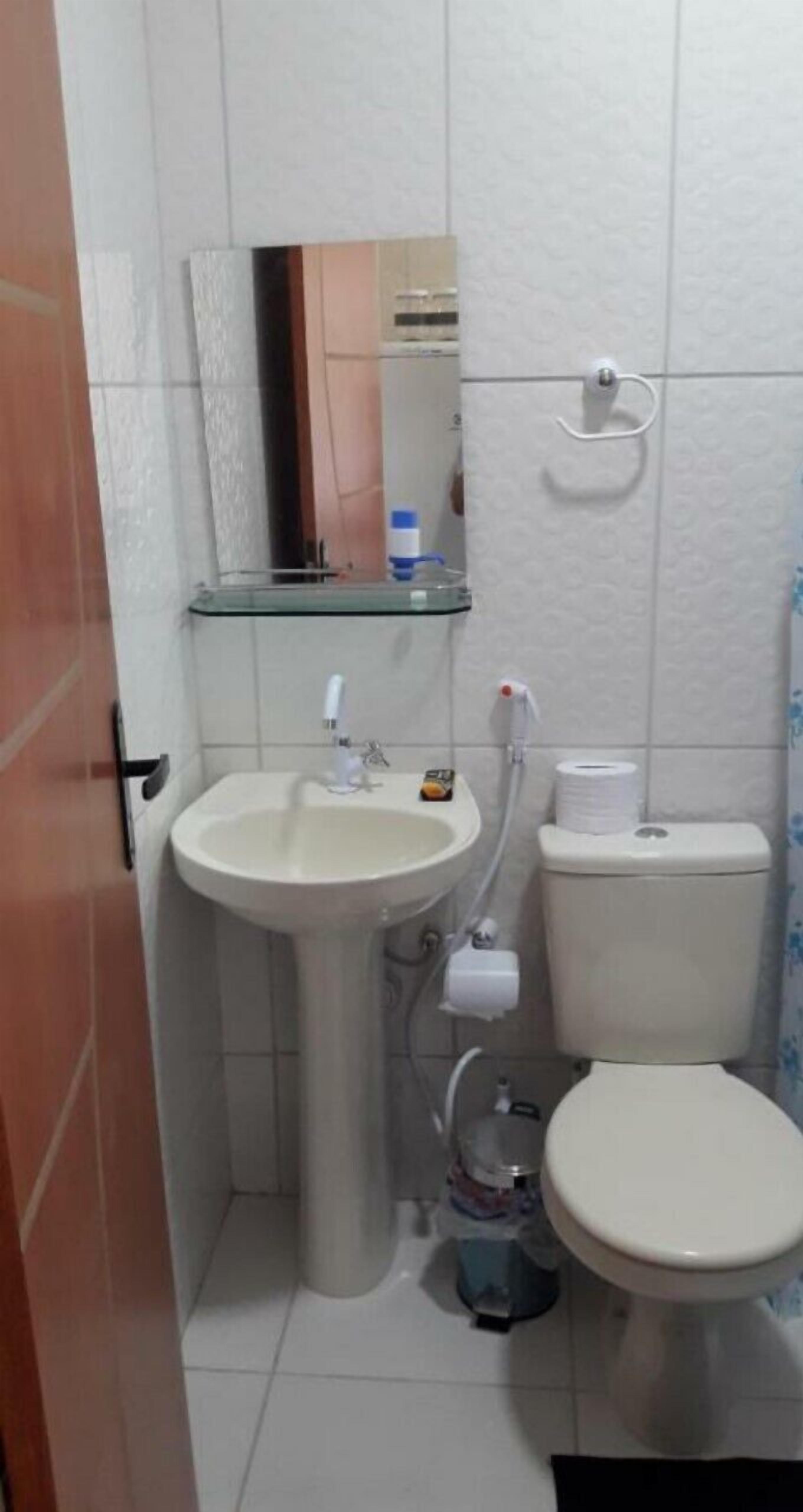 Un baño pequeño con lavamanos pedestal, inodoro y estante de vidrio sobre el lavamanos.