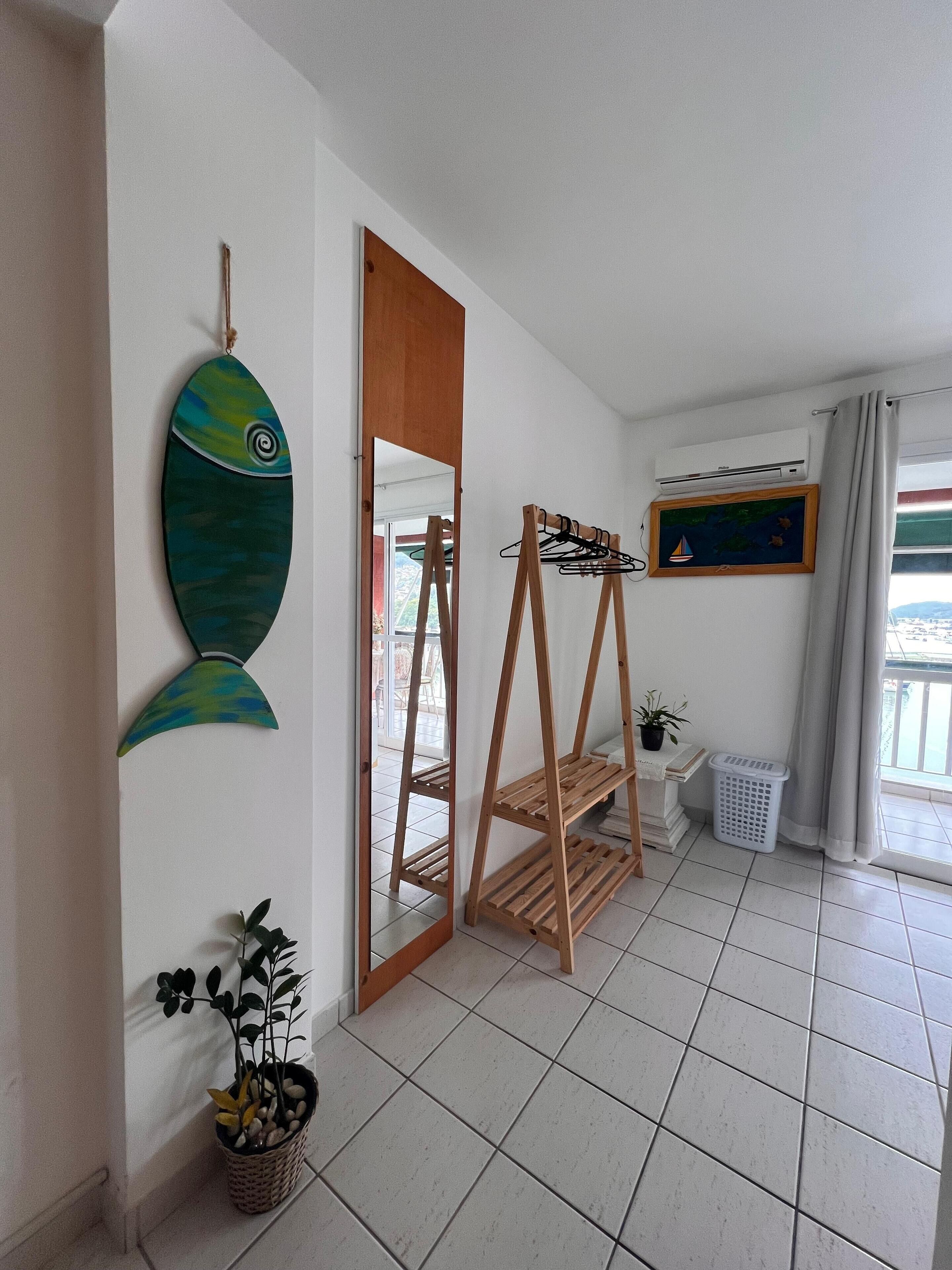 A room with a large mirror, wooden shelves, a potted plant, and a framed picture on the wall.