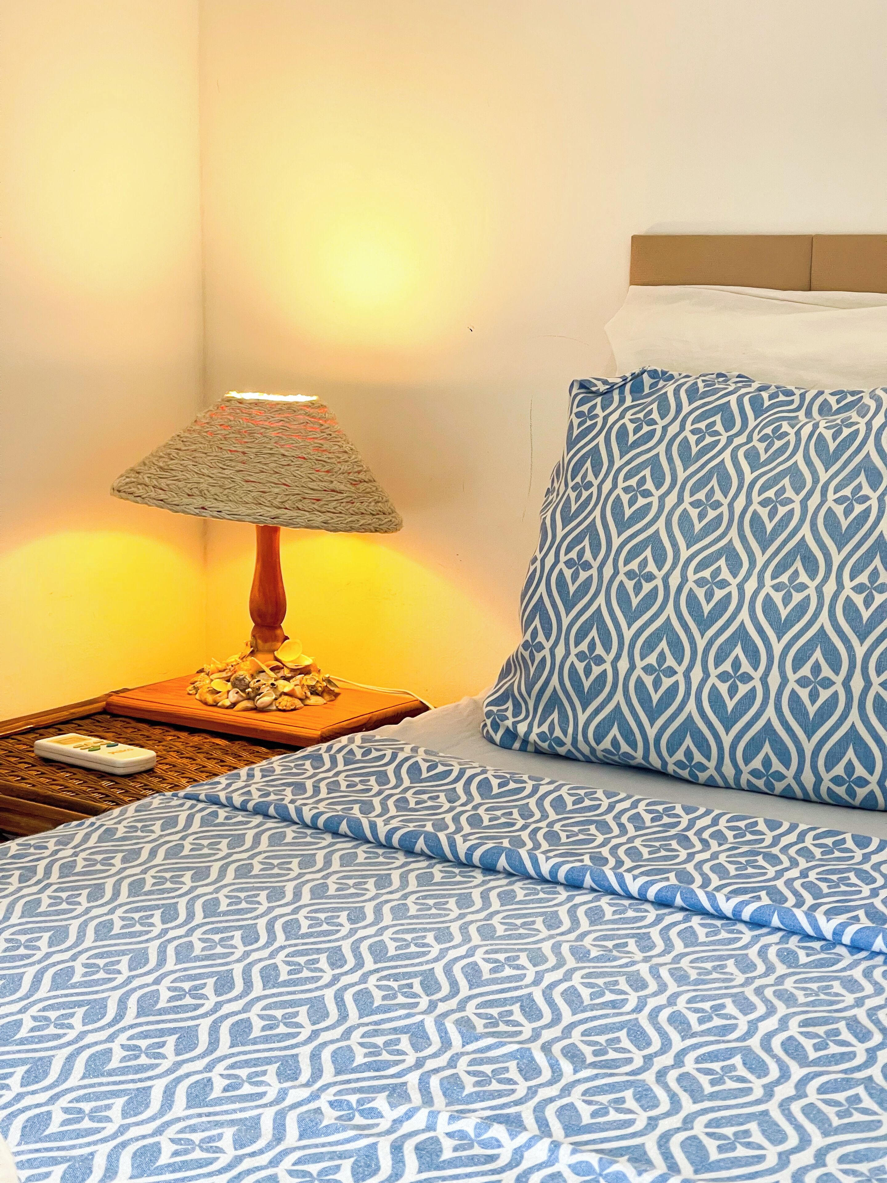 Una cama bien hecha con ropa de cama azul estampada, una lámpara de noche y un cojín con un diseño similar.