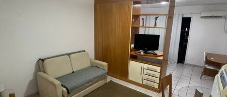 A living room with a sofa, a TV, a wooden cabinet, and a dining area with a chair.