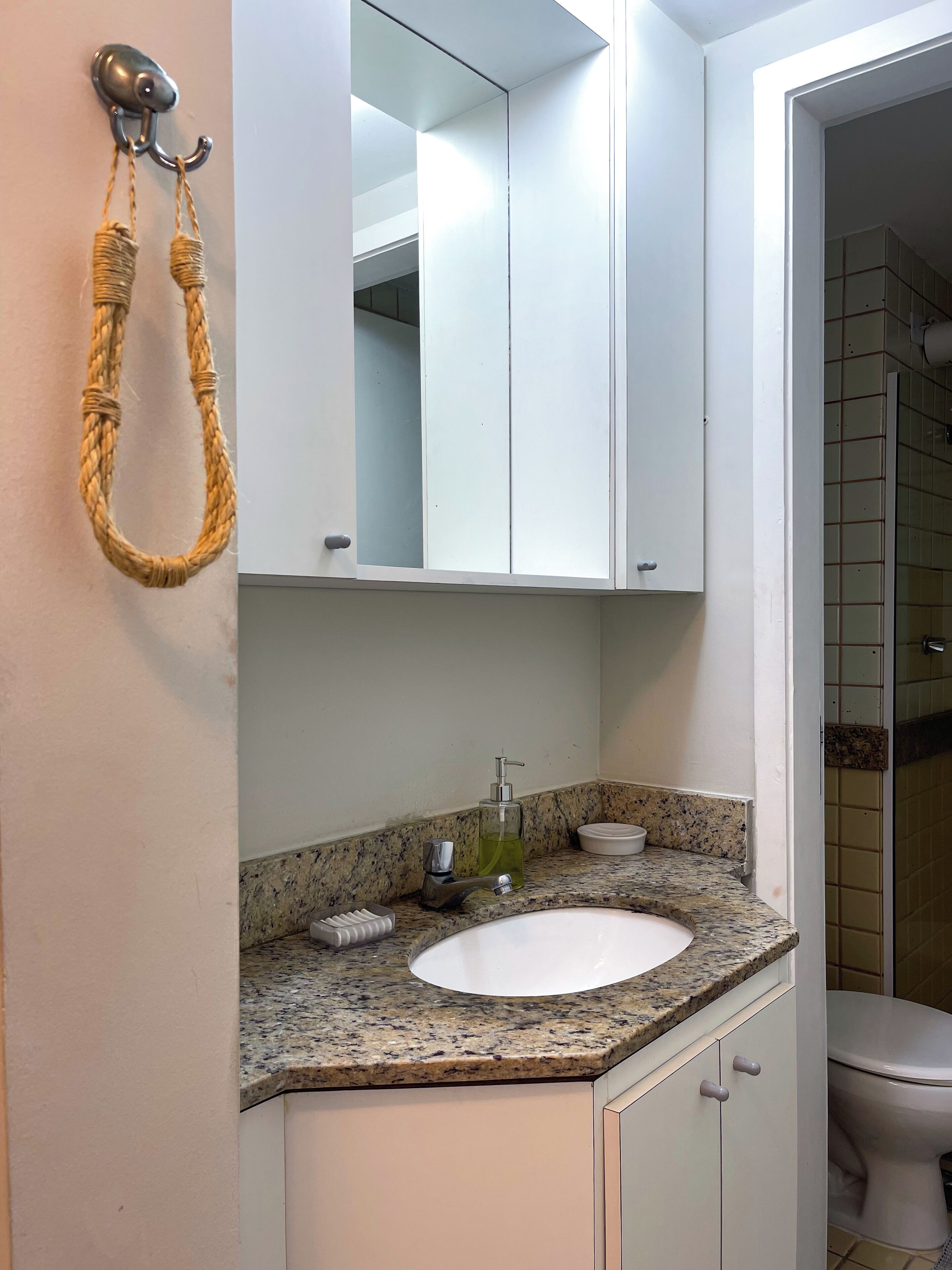A bathroom with a granite countertop, a white sink, a mirror, and a towel rack.