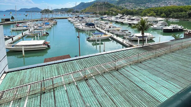 Un puerto deportivo con barcos amarrados, una cubierta de madera y un paisaje montañoso al fondo.