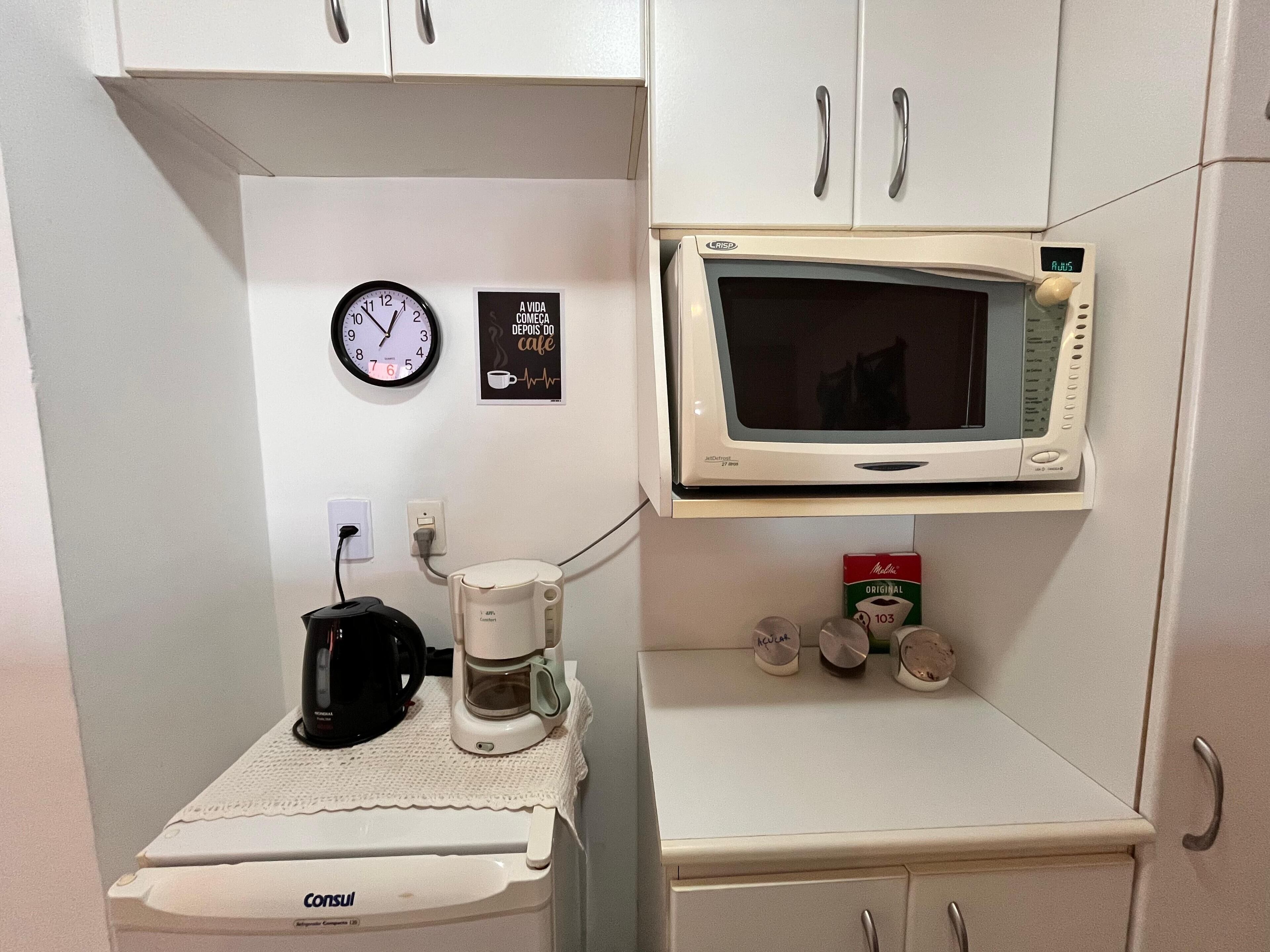 Een kitchenette met een koffiezetapparaat, magnetron en een klok aan de muur.