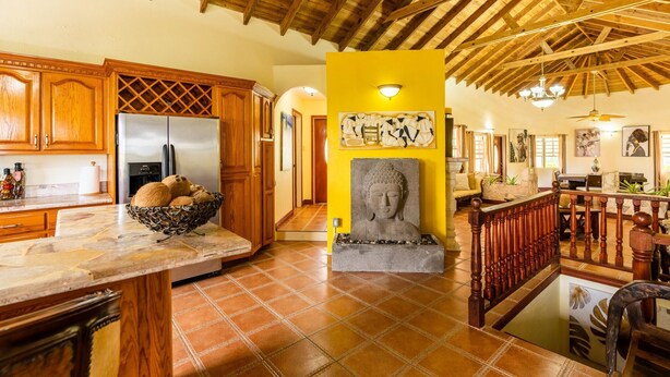A spacious kitchen with wooden cabinets, a large refrigerator, and a stone Buddha statue.
