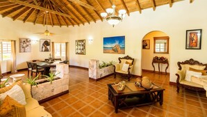 A spacious living area with a high wooden ceiling, a dining table, sofas, and a coffee table with decorative items.