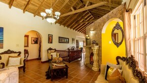 A spacious living room with a high wooden ceiling, a stone fireplace, and a large mirror on the wall.