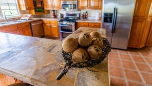 A kitchen with wooden cabinets, a refrigerator, and a stone countertop with a basket of coconuts.