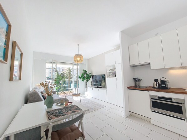 A modern kitchen with white cabinets, a built-in oven, and a dining area with a table and chairs. - N&J - STUDIO RIVIERA - Central - Very close sea (Niza)