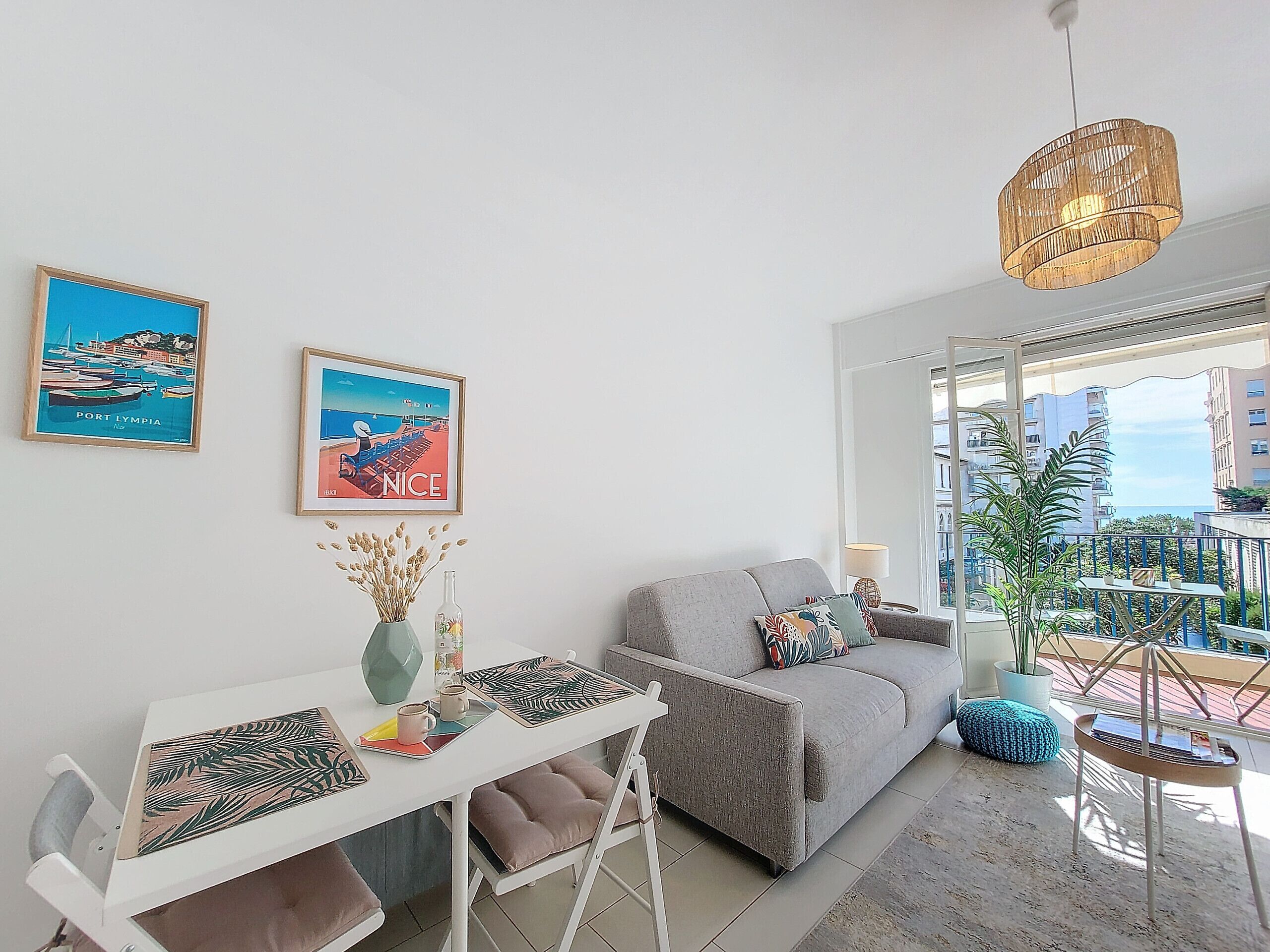 Un salon moderne avec un canapé blanc, une table à manger agrémentée d’un vase et d’une tasse, et deux affiches encadrées accrochées au mur.
