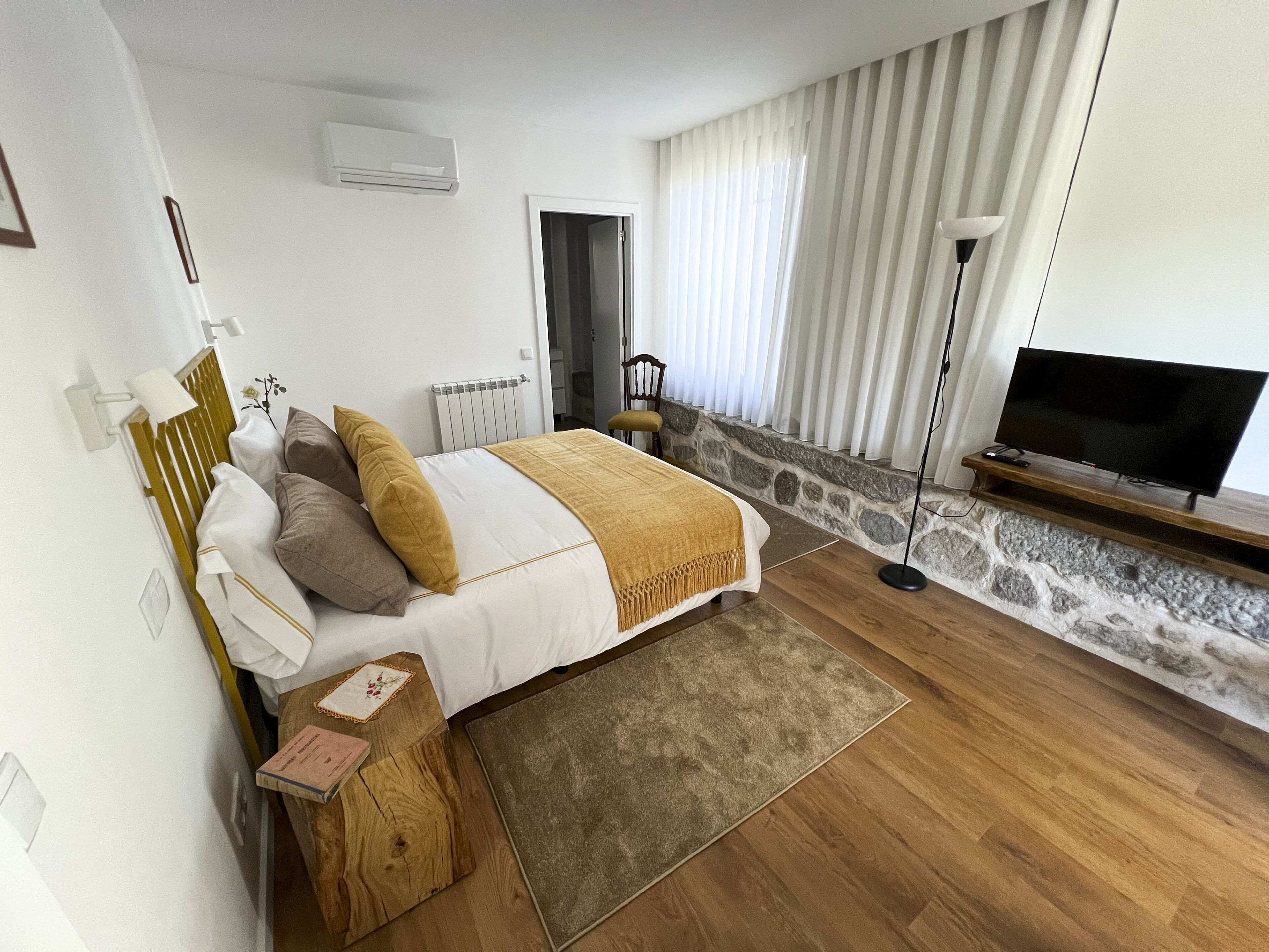 A bedroom with a bed, bedside table, lamp, TV, and stone wall.