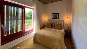 Une chambre à coucher avec un lit, une fenêtre avec des stores, un tableau au mur et un luminaire.
