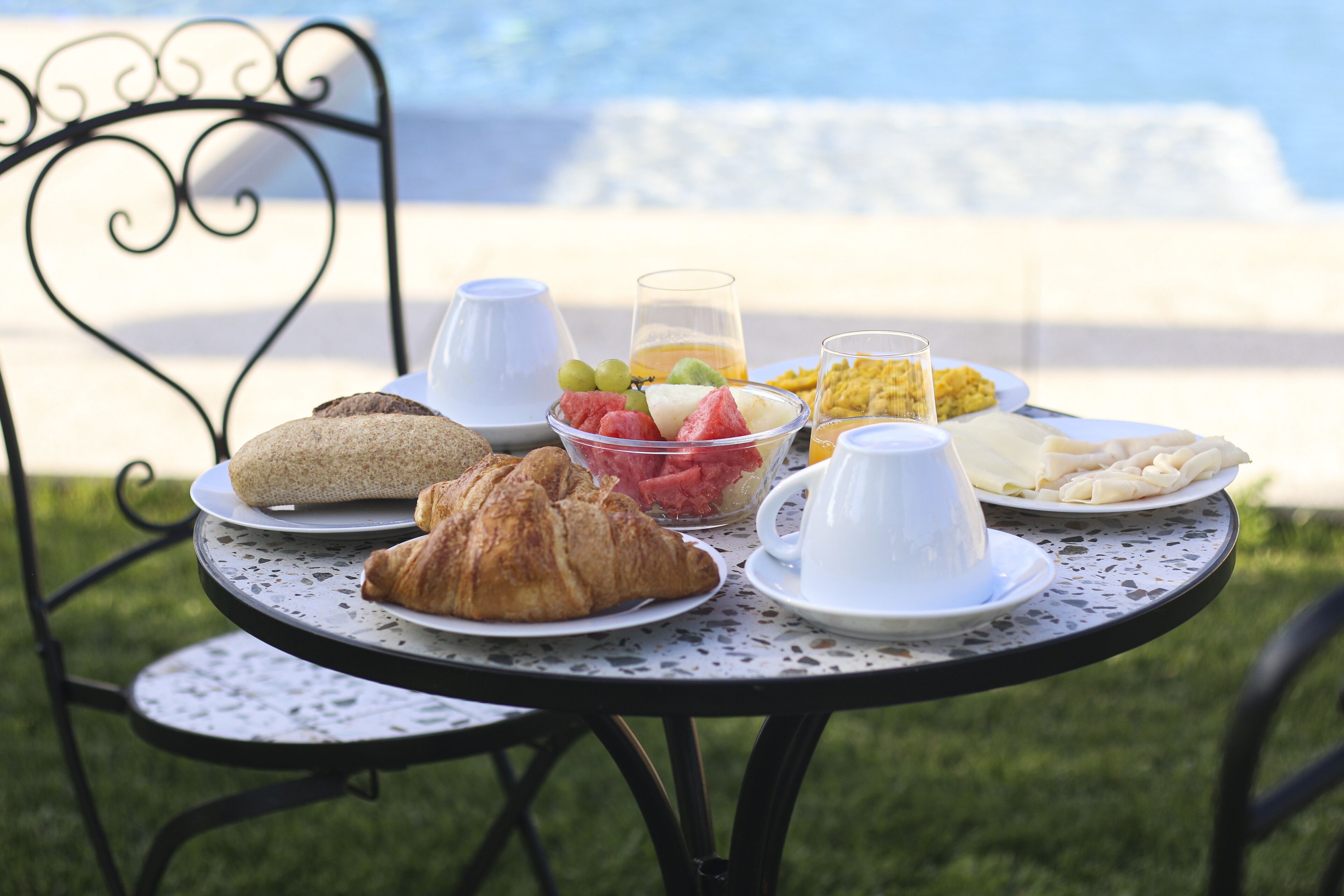Une table dressée pour le petit-déjeuner, avec des croissants, des fruits et des céréales, et une vue sur la mer en arrière-plan.