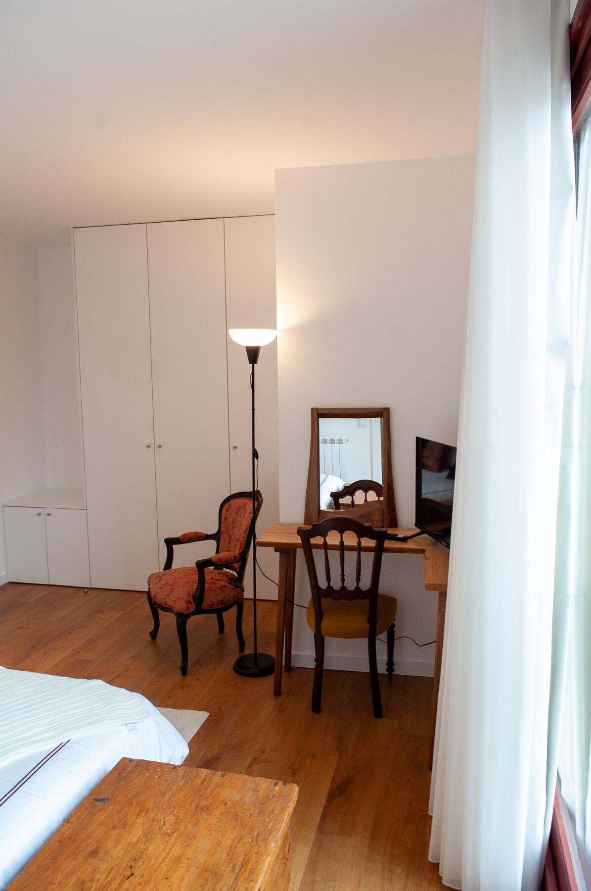 Una habitación con cama, escritorio, dos sillas, una lámpara de pie y un armario.